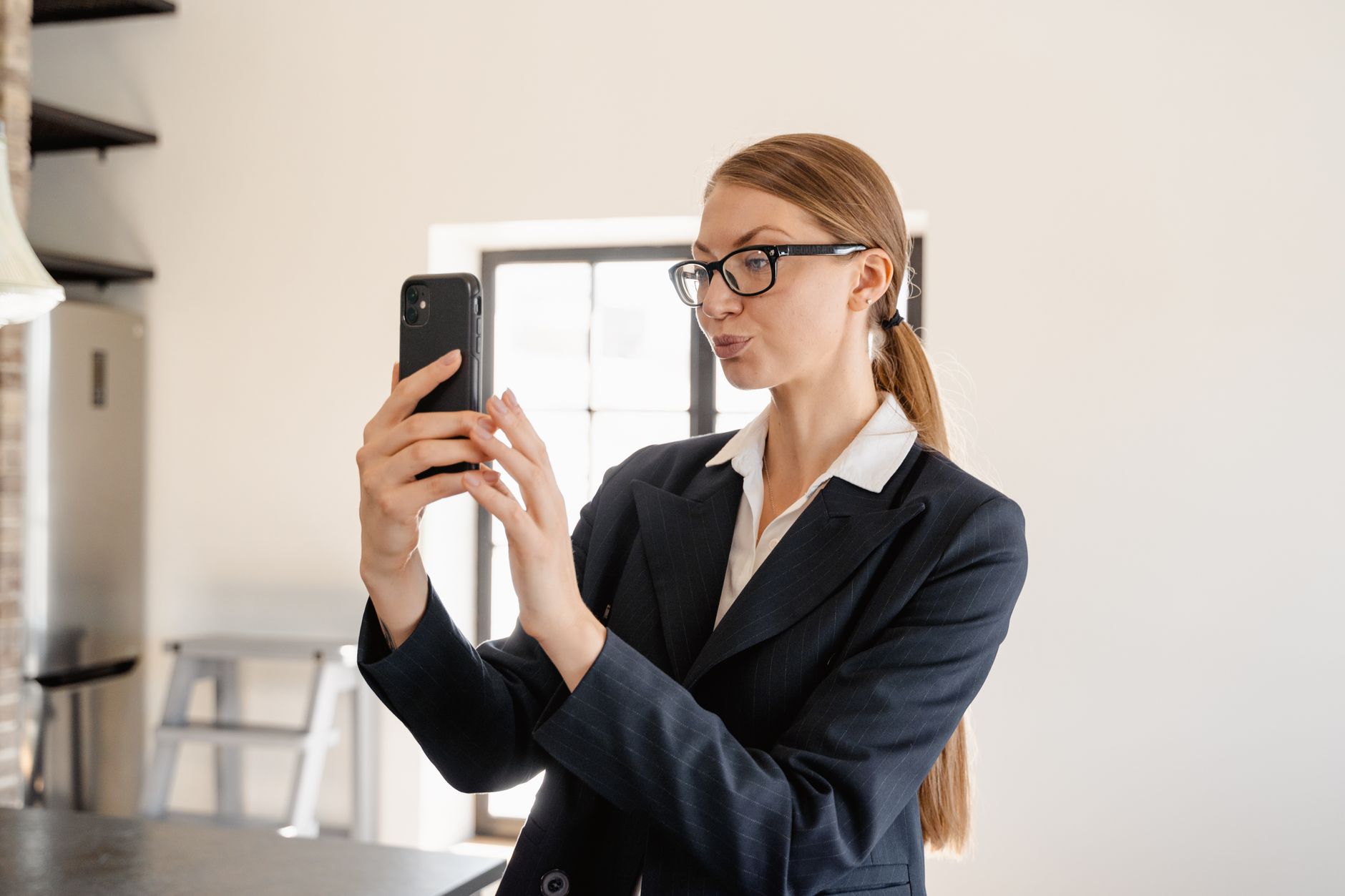 Professional woman in business attire taking a selfie with smartphone indoors.