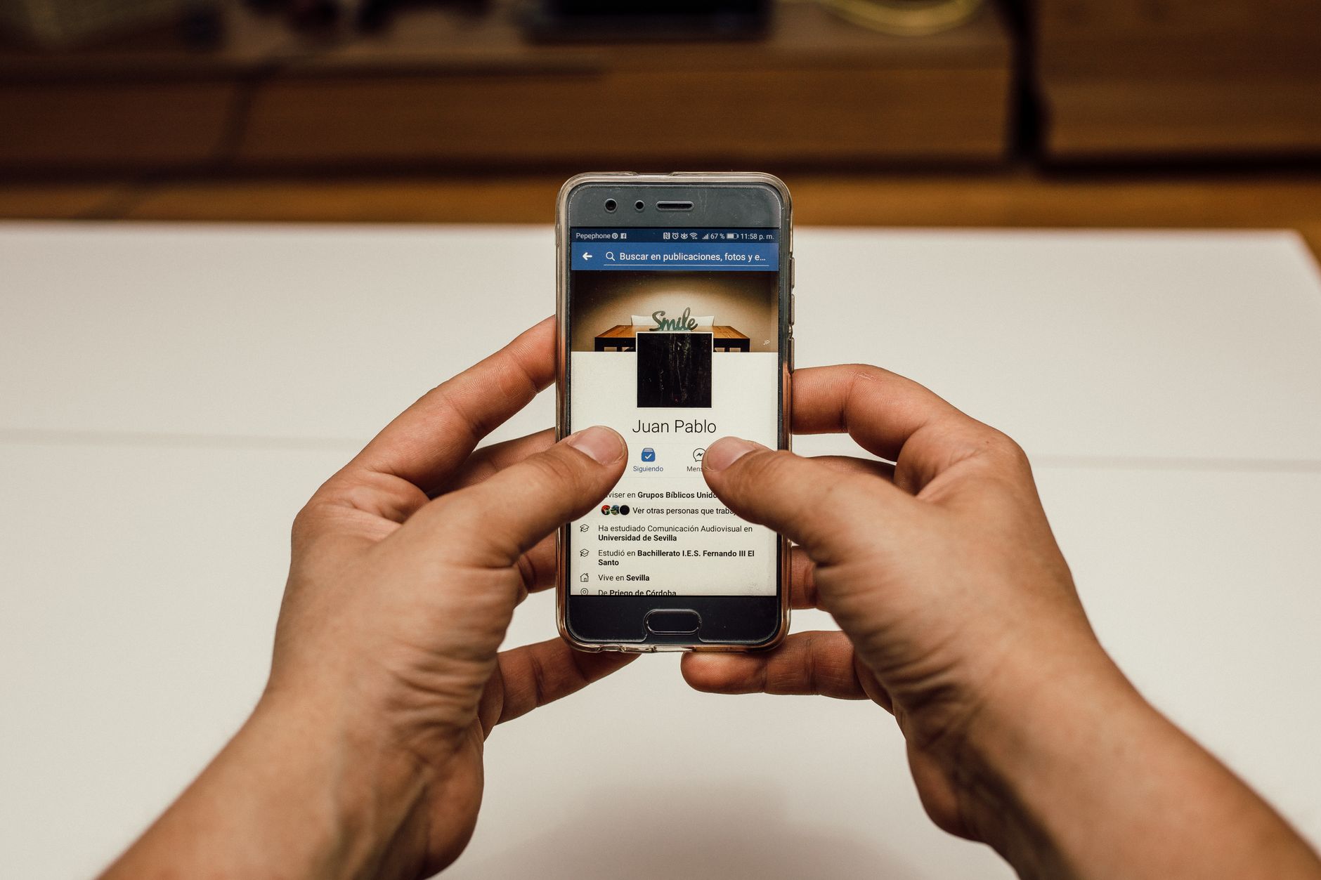 Close-up of hands using a smartphone with a social media page indoors.