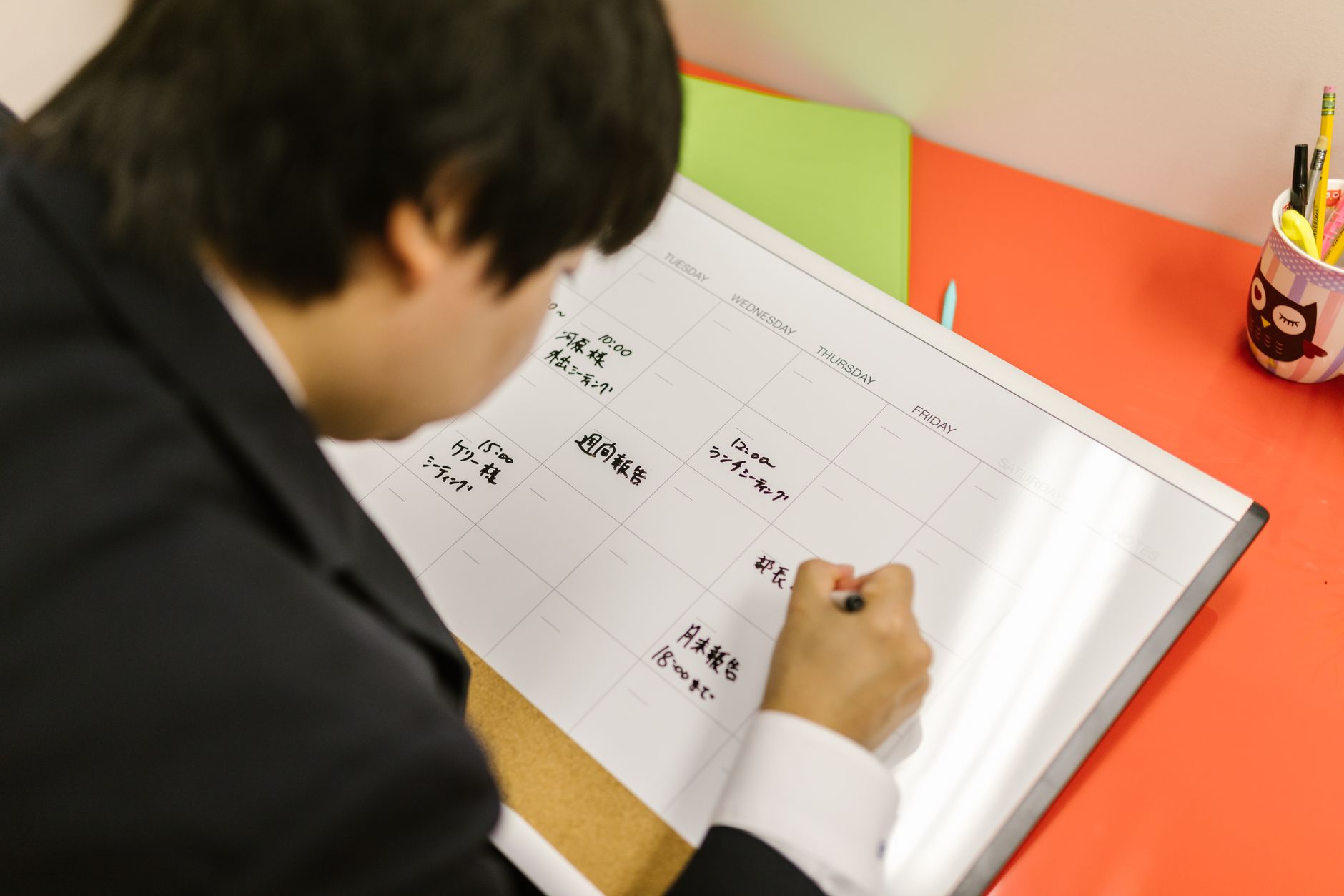 Businessperson writes in a planner on a desk, organizing weekly schedule professionally.